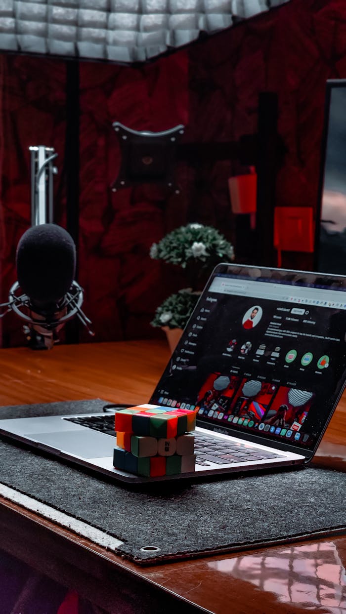Modern office scene with a laptop, Rubiks Cube, and microphone on a desk. Ideal for creative workspace themes.